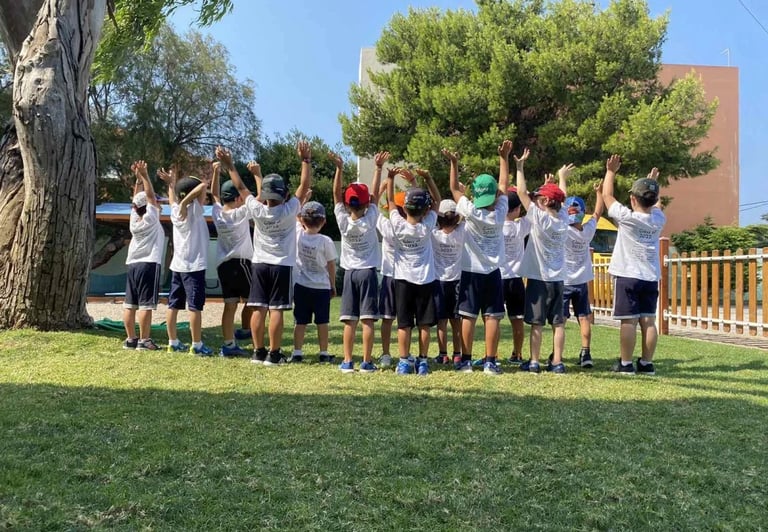 Παιδιά με καλοκαιρινές στολές και καπέλα υψώνουν τα χέρια τους στον αέρα, συμμετέχοντας σε δραστηριό