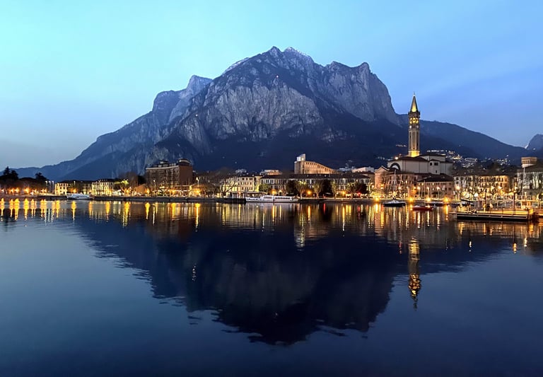 Night view of Lecco on Lake Como, with city lights reflecting on the water and mountain backdrop