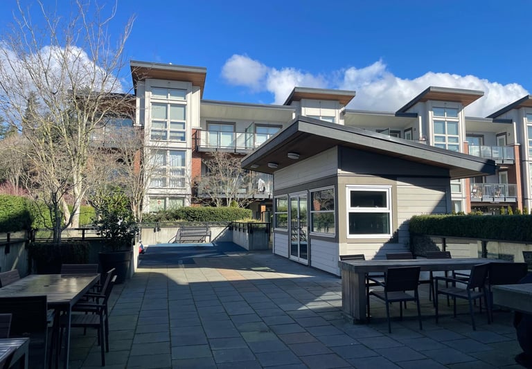 Modern apartment building rooftop patio with outdoor dining tables and a grey clubhouse.