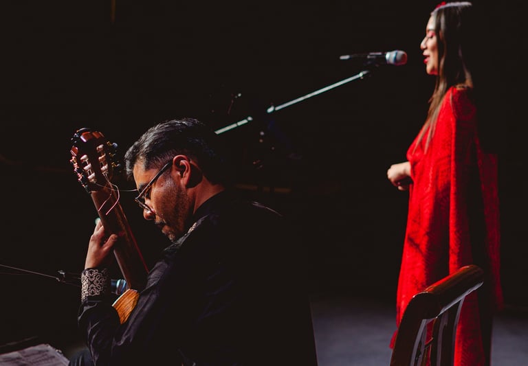 A male guitarist plays acoustic guitar while a female singer in a red dress performs at a live concert.
