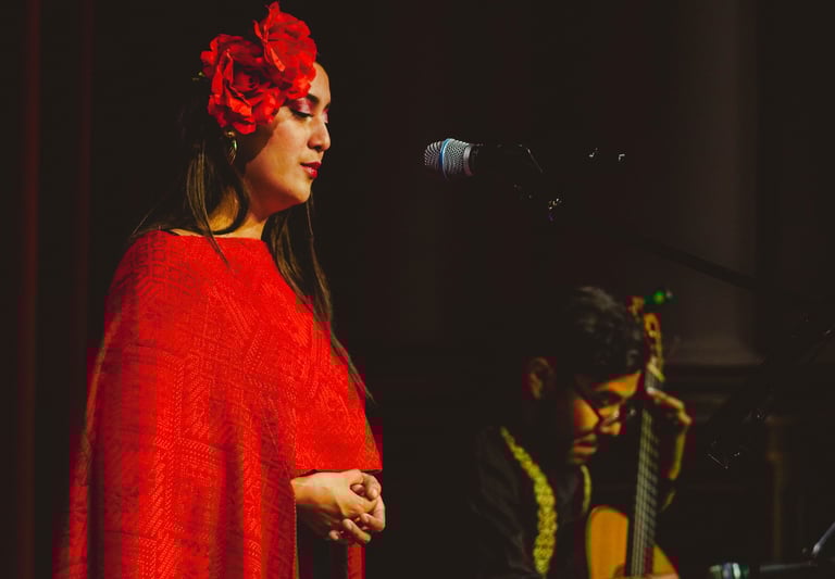Female singer in a red floral headpiece performing live with a Spanish acoustic guitar player.