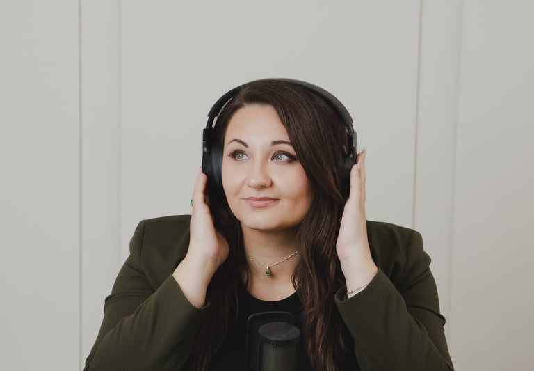 Adriana wearing headphones sits at a desk with a professional microphone recording a podcast.