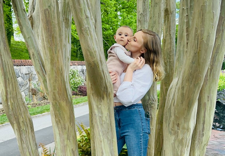A mother holding her baby in a tree, kissing her on the cheek while the baby looks at the camera, showing loving mother-child