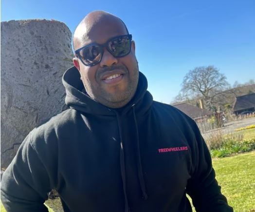 Man outside in a sweater and glasses looks at the camera.