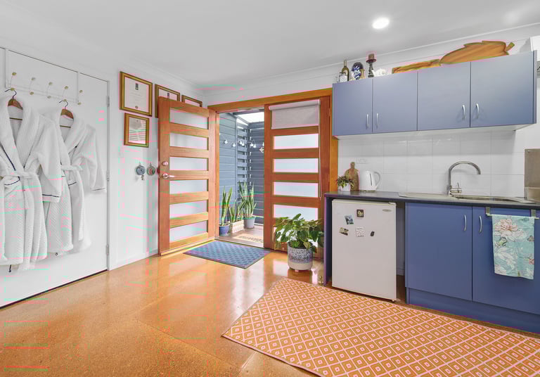 Kitchenette at Marche Home Stay with blue cabinets, a small fridge, bathrobes, and doors opening to a cosy outdoor area.