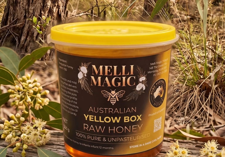 A tub of Melli Magic Australian Yellow Box Raw Honey displayed outdoors next to native eucalyptus blossoms.