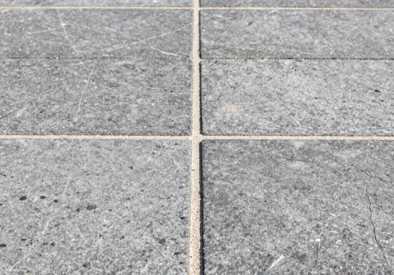 Close-up macro architectural photograph of perfectly aligned gray stone paver joints, clean stabilized sand lines, bright midday sun highlighting the texture