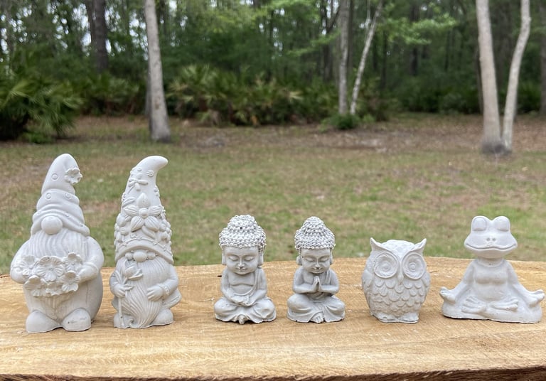 Collection of tiny stone garden figurines including gnomes, meditating Buddhas, an owl, and a frog.