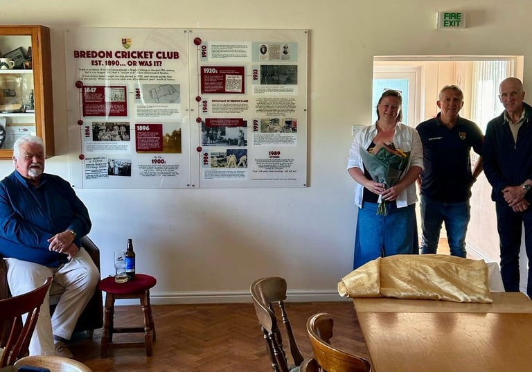 A group of people standing around a wall mounted timeline showing a history of Bredon Cricket Club