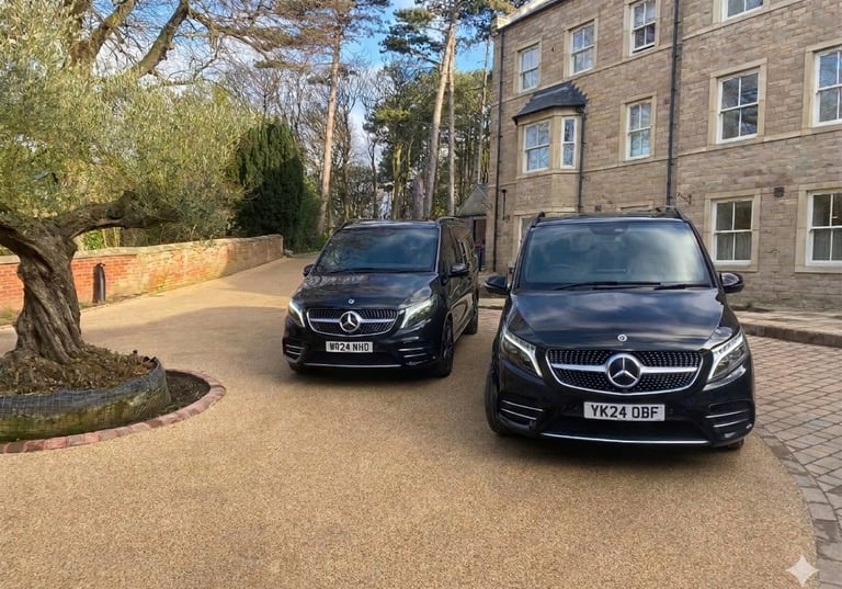 TwoBlack Mercedes-Benz V-Class cars parked on a gravel driveway in front of a stone building.