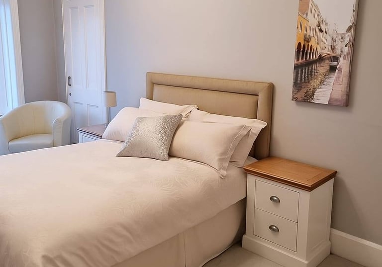 Neutral modern bedroom with a beige upholstered headboard, white bedding, and a Venice canal wall art piece.