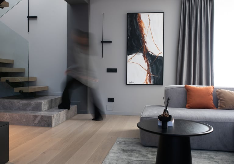 Modern living room interior with grey sofa, abstract wall art, and floating wooden stairs.