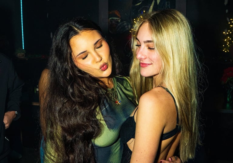 Two young women hugging and posing during a night out at a dimly lit bar or nightclub.