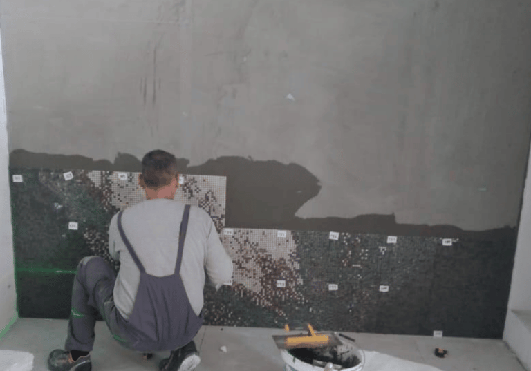 Fliesenleger befestigt nummerierte Glasmosaik-Platten auf vorbereiteter Wandfläche.