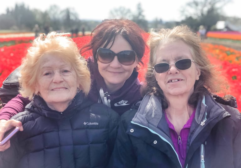 Three happy women wearing jackets and sunglasses smiling in a vibrant red tulip field.