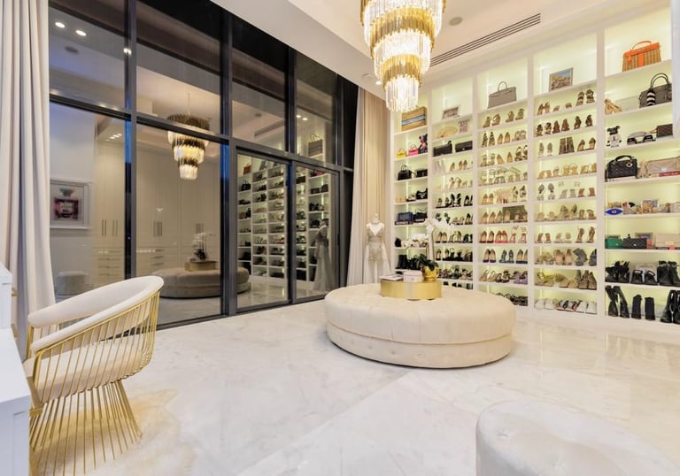 Luxurious walk-in closet with glass doors, shoe wall, and gold chandeliers.