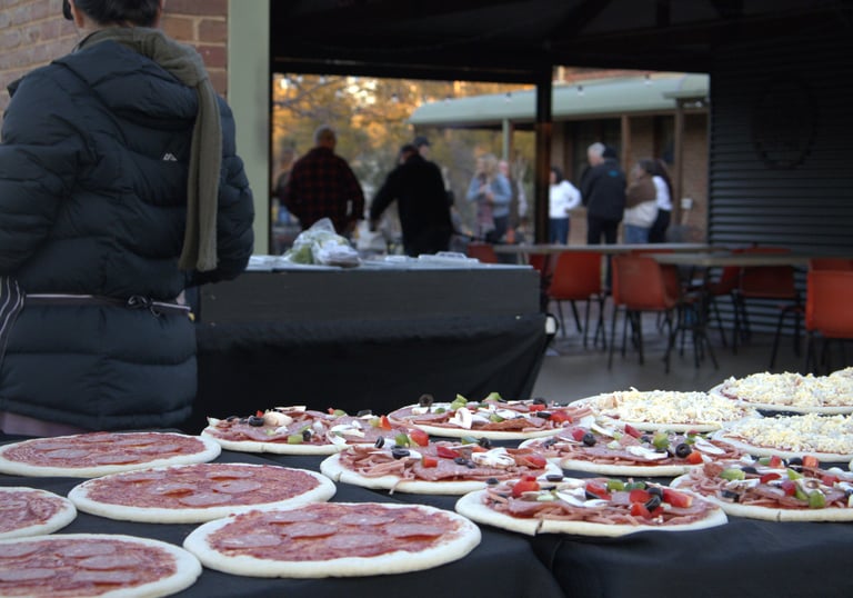 rows of pizzas being prepared by staff. Pizza catering