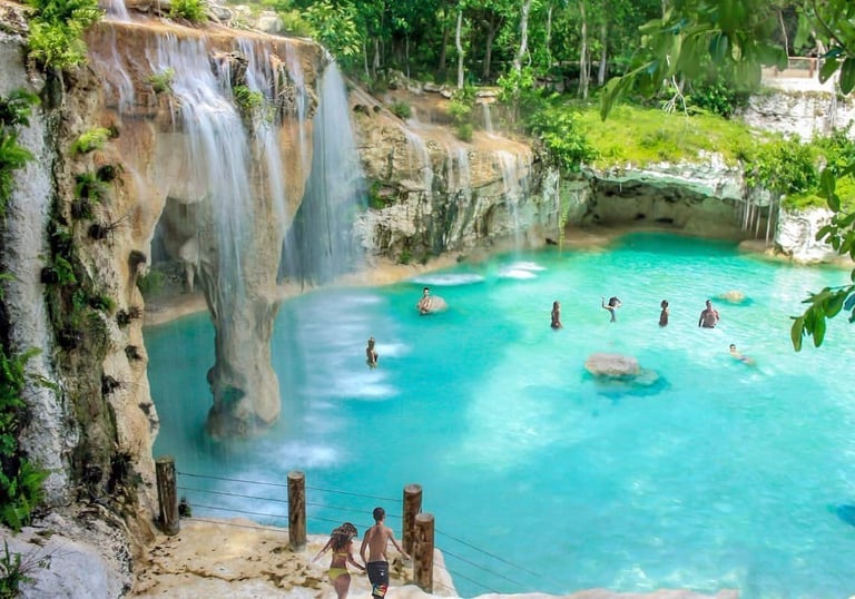 a waterfall in a pool with people swimming in the water scape park punta cana