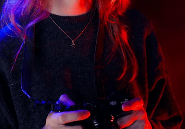 le portrait d'une femme qui tiens un appareil photo avec un jeu de lumière rouge et bleu