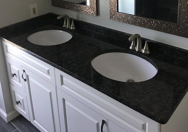 Double vanity with white shaker cabinets, dark countertop, and bronze mosaic mirror frames