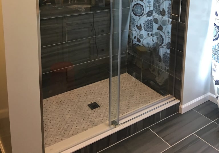 Modern walk-in shower with glass, dark gray tiles, light mosaic floor, stainless steel fixtures