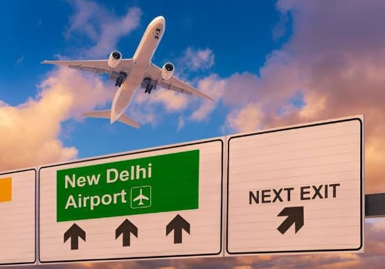 a plane flying over a highway sign new Delhi airport with a plane in the background