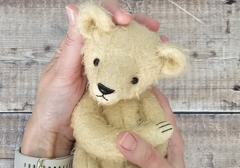 a small, pale handmade teddy bear held in hands