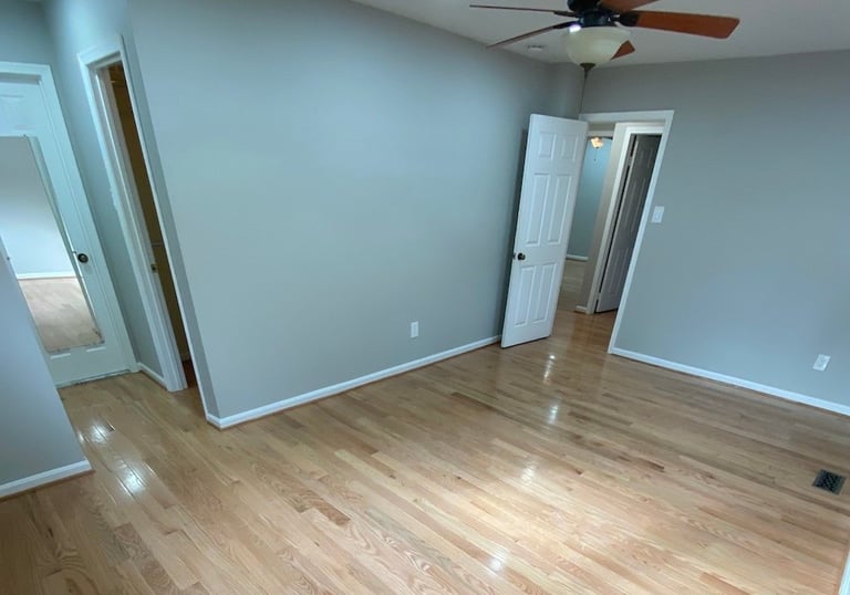 Wide bedroom view showing refinished hardwood flooring and white trim