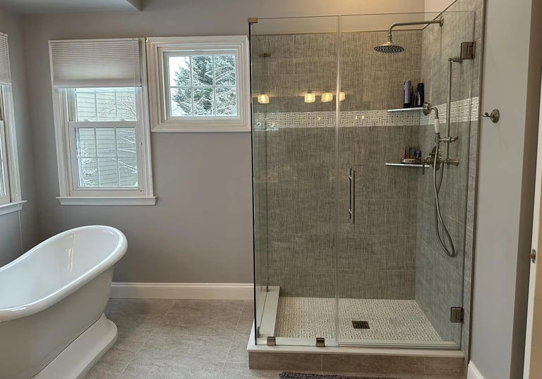 Renovated bathroom with white freestanding bathtub, stainless steel tub filler, and glass shower