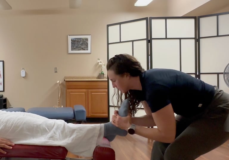 Chiropractor adjusting patient's foot while patient lays on back on chiropractic table.
