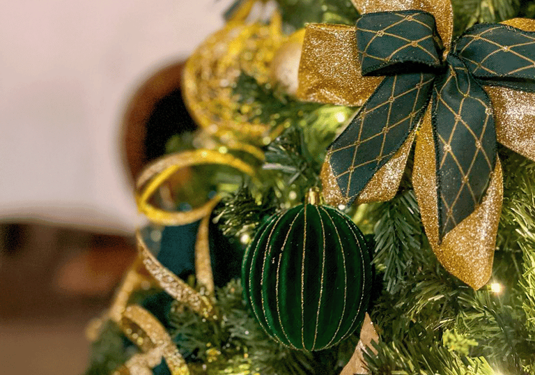 Uma árvore de Natal com um laço verde e dourado e uma bolinha verde