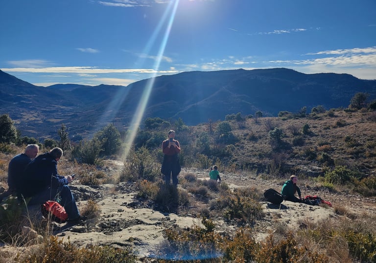 a group of people sitting and relaxing on a hill with a sun shining in the background