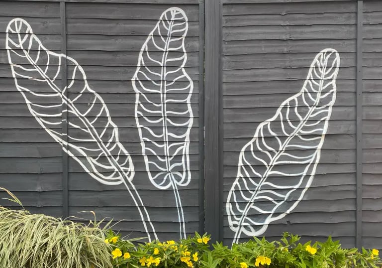 Modern graphic mural of three large tropical leaves on grey yard fence with flowers, by House of Lyr