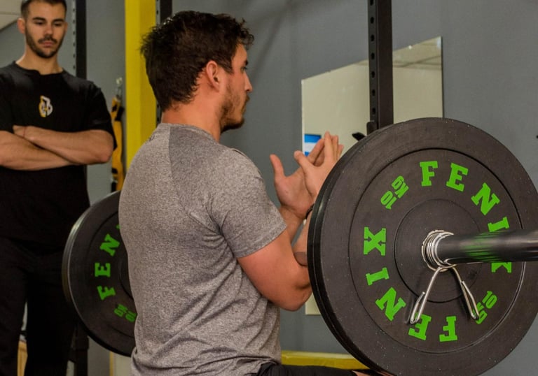 a man squatting on a barbEL WITH HIS PERSONAL TRAINER ON HIS SIDE