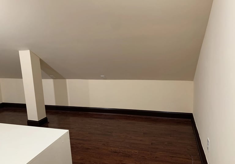 Empty attic room with new dark hardwood floors, light beige walls, and sloped ceiling
