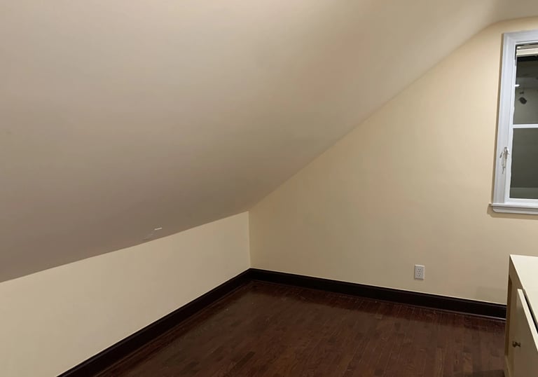 Renovated attic room with light beige painted walls, dark floors, and sloped ceiling