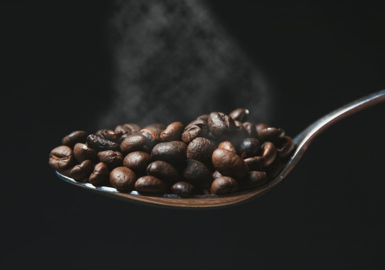 A spoon with freshly roasted coffee beans with fresh smoke visible