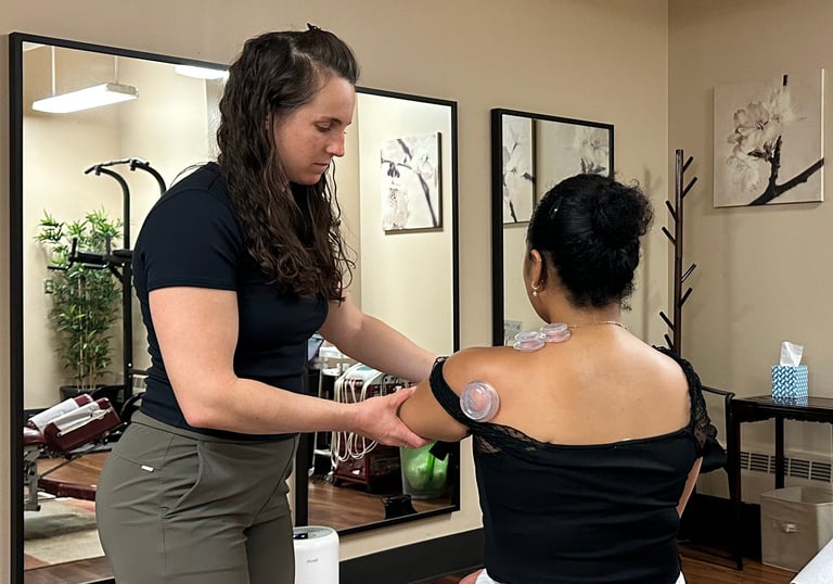 Chiropractor cupping a patient's shoulder and assisting movement with treatment room in background.