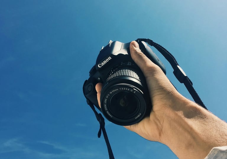 a person holding a camera and taking a picture with a bright blue sky