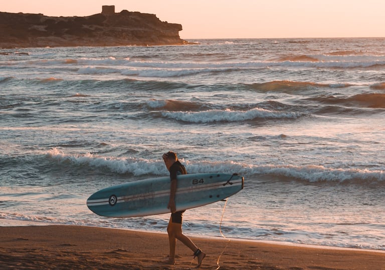 Surfer at sunset on Porto Ferro beach, Sassari, Sardinia, one of the island’s top surf spots.