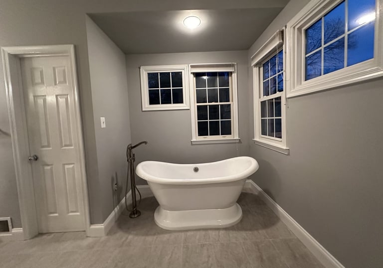 close-up of freestanding bathtub with stainless steel floor-mounted tub filler and windows