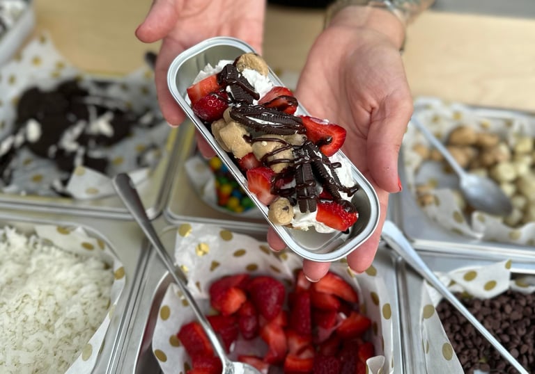 a person holding dessert in front of a table filled with toppings
