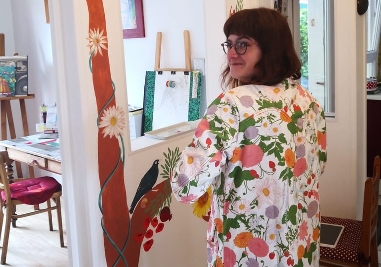 Photo de l'artiste-peintre Marie Hardy devant une fresque d'arbre réalisée dans le salon d'un particulier en Normandie