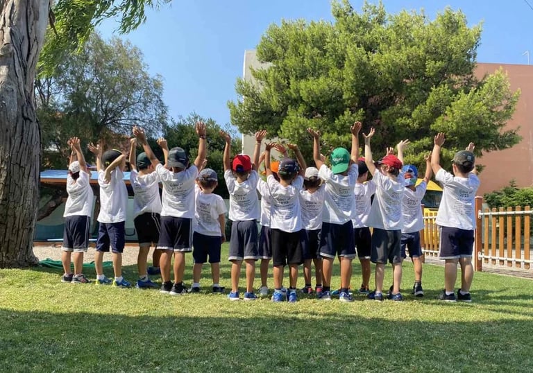 Παιδιά με καλοκαιρινές στολές και καπέλα υψώνουν τα χέρια τους στον αέρα, συμμετέχοντας σε δραστηριό