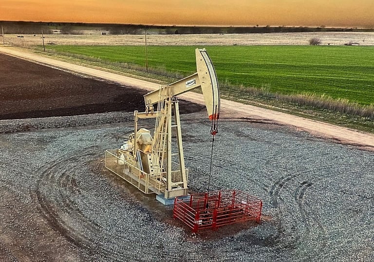 An oil pump jack operates in a rural field during a golden sunset, representing energy production.
