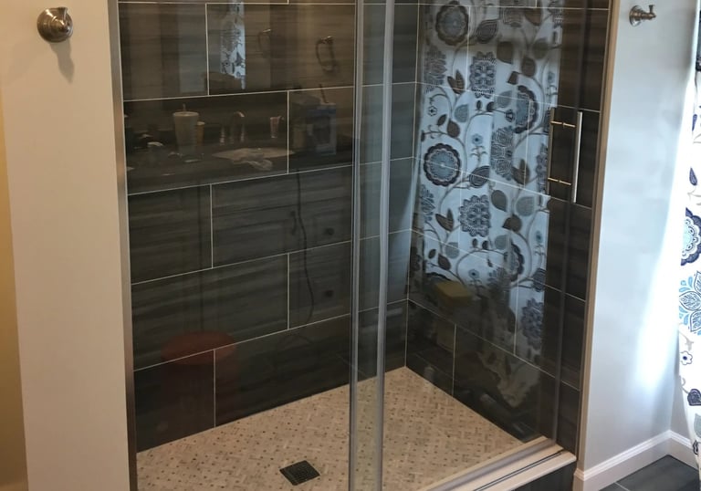 Modern walk-in shower with glass, dark gray tiles, light mosaic floor, stainless steel fixtures