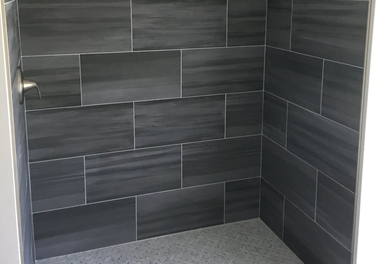 Walk-in shower with dark gray wall tiles, light gray mosaic floor, and stainless steel fixtures