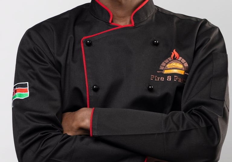 A smiling young chef wearing a professional black double-breasted culinary jacket with red trim.
