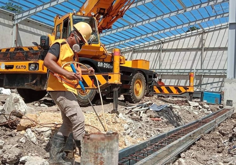 A construction worker in safety gear works near a Kato crane at an industrial building site.
