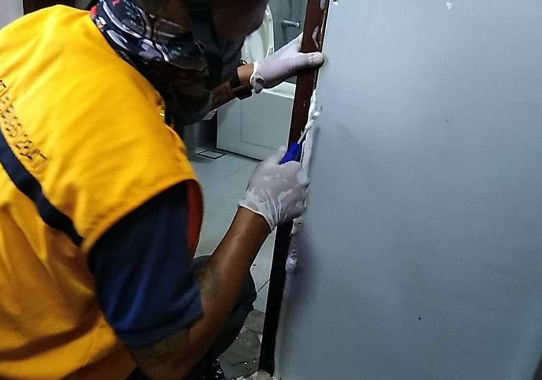 Professional technician applying white silicone sealant to a door frame during bathroom repairs.